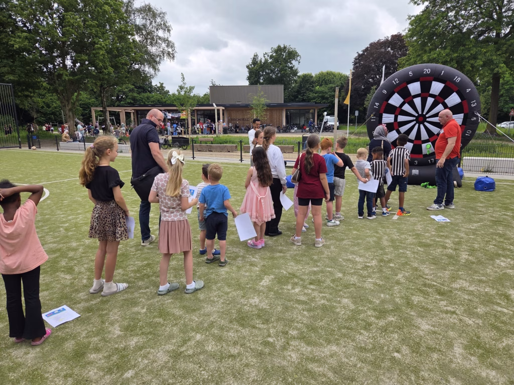 Kinderen staan in de rij bij het grote opblaasbare dartbord op de Buitenspeeldag 17 juni 2026 in Oldenbarneveld Bijschrift: Het reusachtige dartkussen was één van de trekpleisters op 17 juni. Geduldig in de rij — iedereen wilde een beurt.